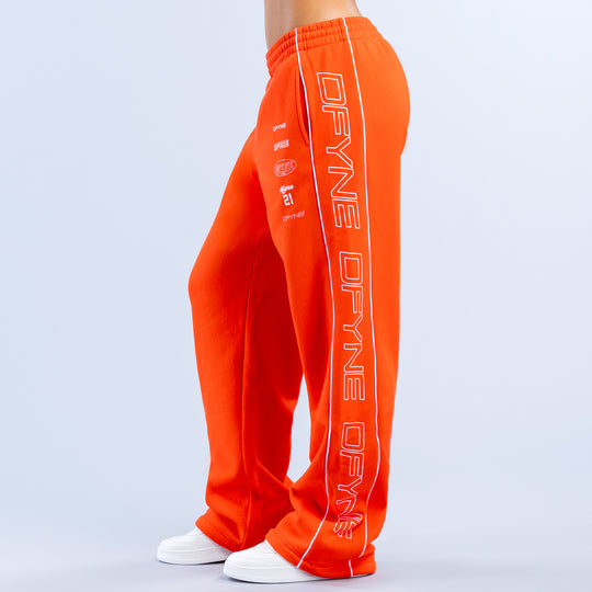 Orange wide-leg joggers with vertical printed side lettering, elastic waistband