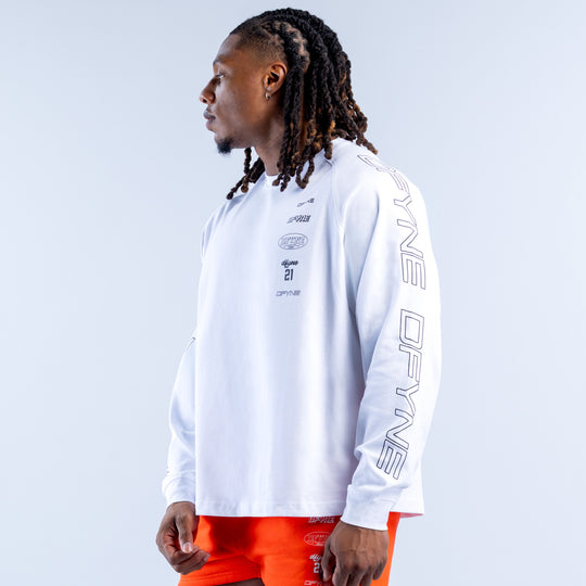 White long-sleeve kids top with chest emblem and vertical sleeve logo; orange shorts