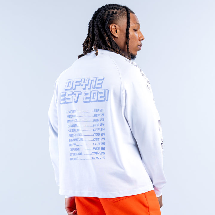 White long-sleeve kids top with blue back schedule print; orange shorts visible